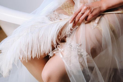 Close-up of a white feather lying on the feet of a bride dressed in boudoir underwear, The morning of the bride.