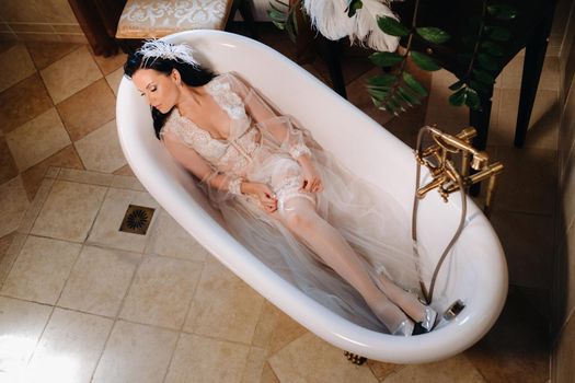 the bride, dressed in a boudoir transparent dress and underwear, lies in a vintage bathroom. Morning of the bride.