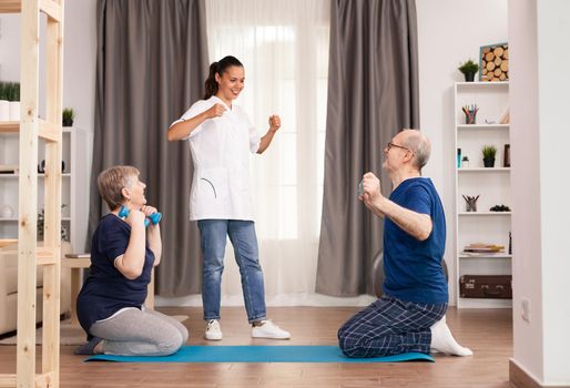 Doctor encouraging his patients to exercise for recovery. Home assistance, physiotherapy, healthy lifestyle for senior old person, training and recovery with professional physiotherapist using dumbbells, resistance band and yoga mat.