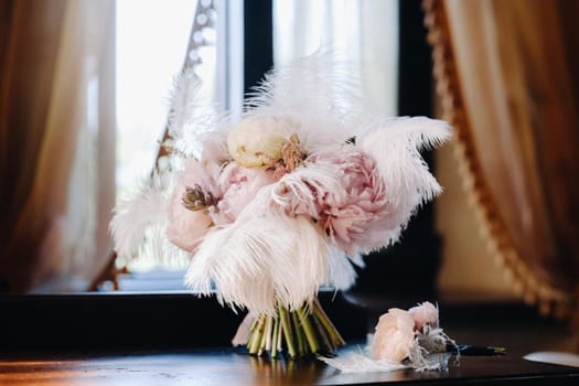 The bride's wedding bouquet of roses decorated with white feathers and a boutonniere.