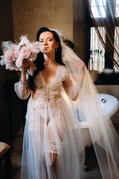 the bride, dressed in a boudoir transparent dress and underwear, sits near a vintage bath with a feather in her hands, The morning of the bride.