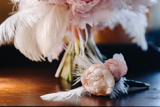 The bride's wedding bouquet of roses decorated with white feathers and a boutonniere.