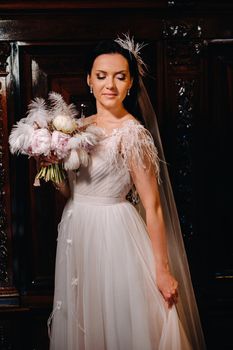 The bride in a wedding dress and with a bouquet stands at the old interior of the castle.