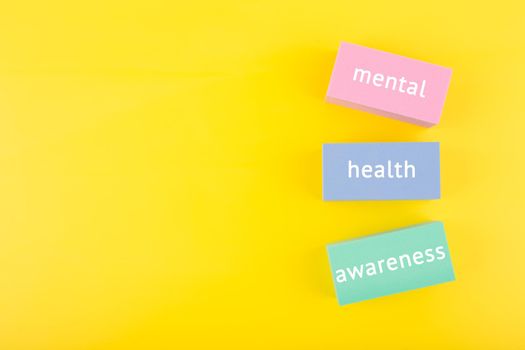 Mental health awareness concept on yellow background with copy space and with text written on colorful tablets. Concept of mental health, self care and psychological issues