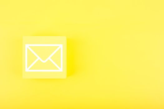 Email marketing, newsletter, promotion information and virtual communication concept. Envelope drawn on small toy cube against bright yellow background with copy space. 