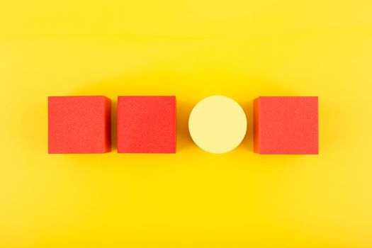 Red toy cubes and yellow circle in a row on bright yellow background. Concept of individuality, being different from others, leadership or unique ideas 
