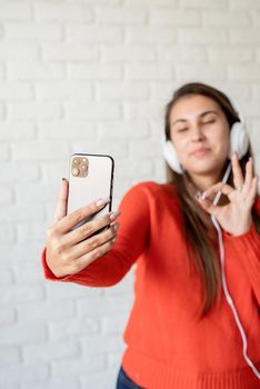 Social media. Young caucasian woman wearing earphones chatting on mobile showing okay sign