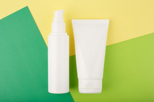 Cosmetic products in white unbranded tubes on green and yellow paper. Set of face cream, lotion or gel for skin cleaning, exfoliating, moisturizing and nourishing