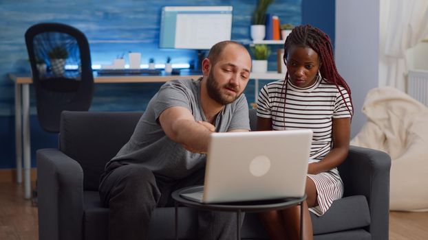 Modern interracial couple doing taxes with laptop and notebook in living room. Multi ethnic partners calculating tax money and budget for financial planning and bills payment at home