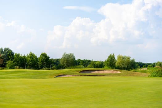 Green grass and woods on a golf field with sand trap