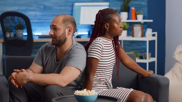 Angry interracial couple having relationship problems at home. Irritated multi ethnic partners fighting while sitting together on couch. Mixed race people having argument in living room