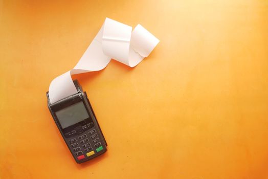 POS machine and long roll paper on orange background .