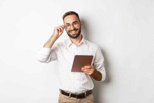 Confident business man working on digital tablet, smiling happy, standing over white background.