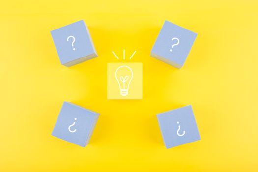 Concept of idea, creativity, start up or brainstorming. Light bulb and question signs drawn on toy cubes on yellow background 