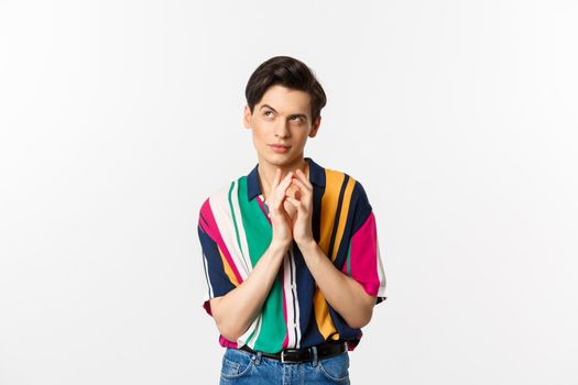 Devious young man having a plan, steeple fingers and looking cunning at upper left corner, scheming something, standing over white background.