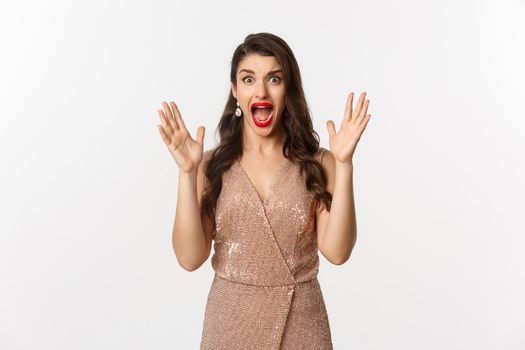 Celebration and party concept. Beautiful woman in elegant dress screaming and staring at camera scared, looking at something scary, standing over white background.
