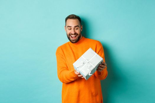 Holidays and celebration concept. Excited man receiving gift, looking happy at present and smiling, standing over blue background.