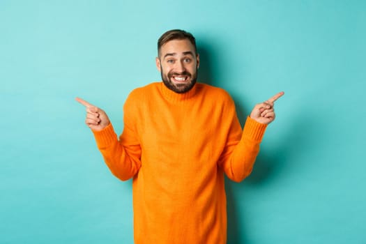 Confused handsome man shrugging indecisive, pointing fingers sideways, cant choose between two variants, standing against light blue background.