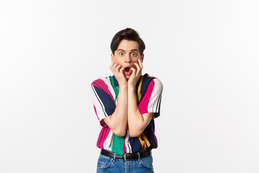 Shocked young man drop jaw, staring at camera impressed and speechless, standing over white background.