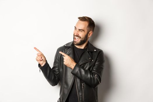 Confident macho man in black leather jacket, pointing fingers left at promo offer, showing logo, white background.