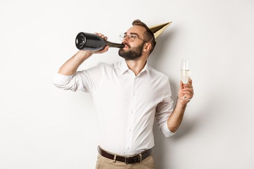 Celebration and holidays. Man drinking chamapgne from bottle on birthday party, standing against white background.