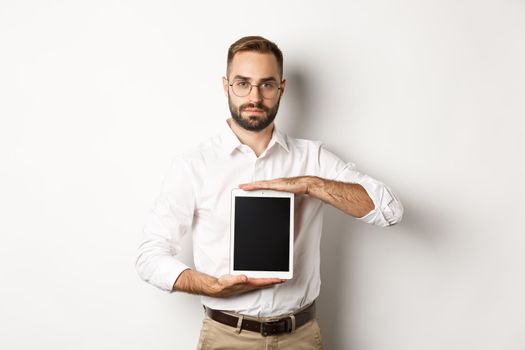 Confident bearded man showing digital tablet screen, demonstrating app, standing over white background.