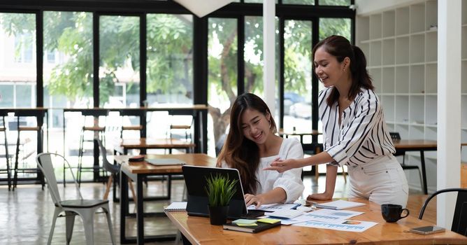 Friendly female colleagues having good relationships, pleasant conversation at workplace, smiling young asian woman listen talkative coworker, discussing new project, talking in office.