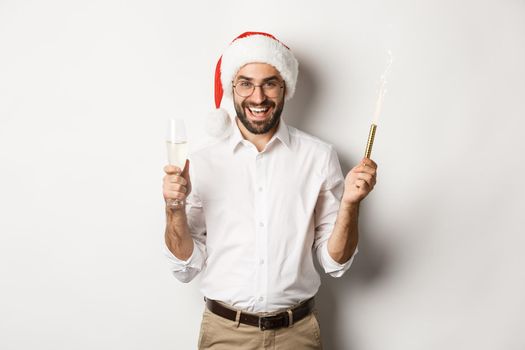 Winter holidays and celebration. Handsome bearded man having New Year party, holding firework sparkle and champagne, wearing santa hat, white background.