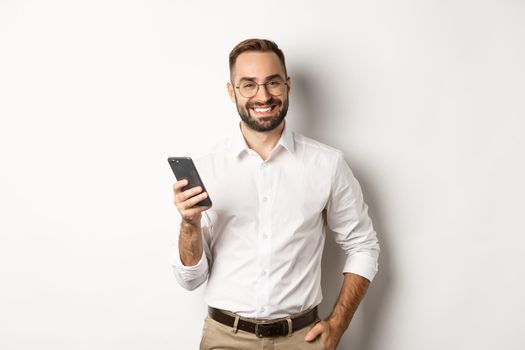 Handsome manager using smartphone and smiling pleased, sending text message, standing over white background.