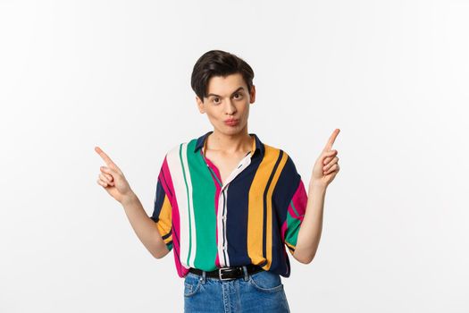 Handsome gay man pointing fingers sideways, showing two variants, demonstrate promos, standing over white background.