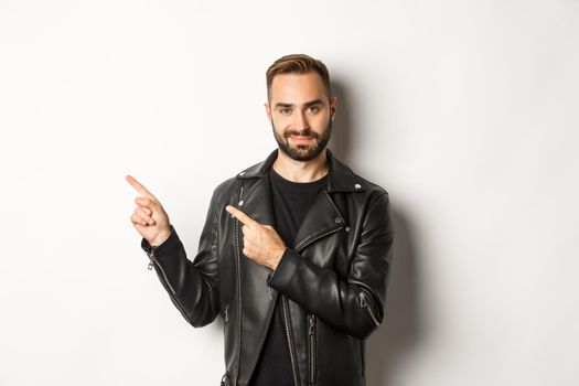 Confident macho man in black leather jacket, pointing fingers left at promo offer, showing logo, white background.