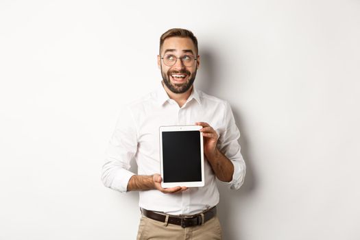 Shopping and technology. Thoughtful man showing digital tablet screen, looking at upper left corner and thinking, standing over white background.