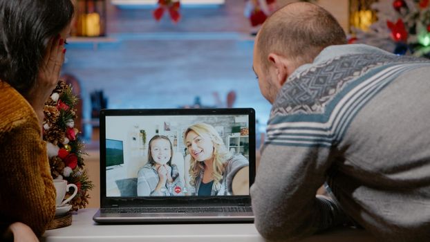 Festive couple talking to family on video call conference for christmas eve festivity. People chatting with woman and little girl using laptop for remote communication on holiday season