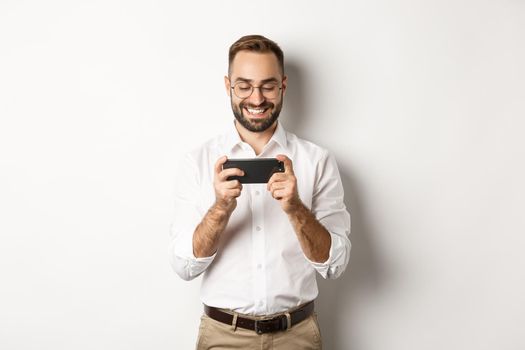 Happy businessman watching video on mobile phone, standing over white background.