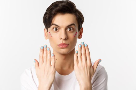 People, lgbtq and beauty concept. Beautiful gay man showing blue nail polish on fingernails and looking at camera, have manicure, standing over white background.