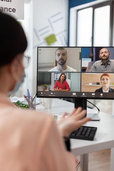 Executive manager with medical face mask discussing management statistics with remote team having online videocall meeting conference on laptop working in startup office. Teleconference on screen