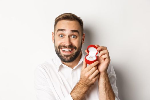 Close-up of handsome guy making proposal, looking hopeful and showing wedding ring, asking marry him, white background.