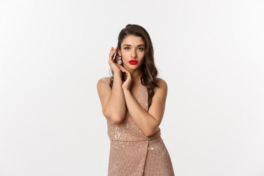 Christmas party and celebration concept. Beautiful and sensual woman in glamour dress, touching her face and posing over white background.