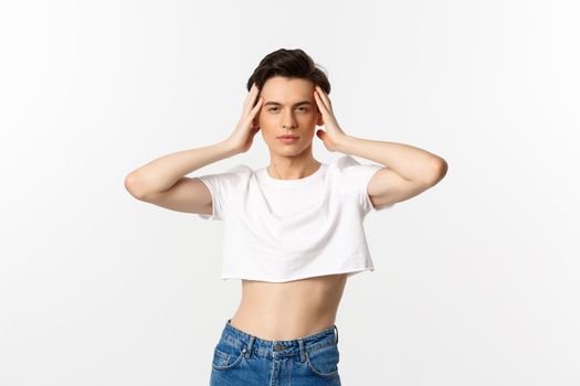 Lgbtq and pride concept. Beautiful and confident gay man wearing crop top, touching face and looking sassy at camera, standing over white background.