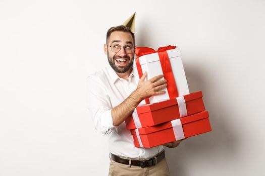 Holidays and celebration. Excited man having birthday party and receiving gifts, looking happy, standing over white background.
