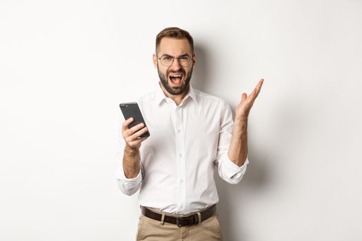 Frusteated man using mobile phone and looking disappointed, complaining, standing over white background.