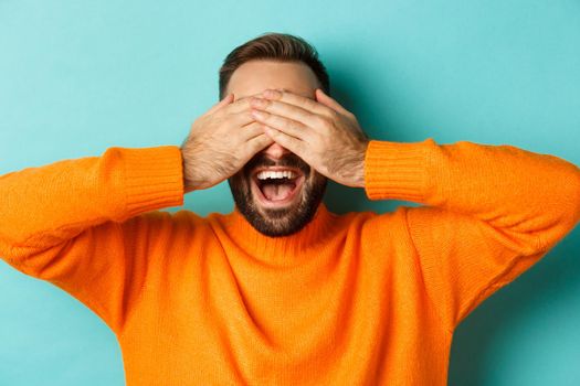 Close-up of happy caucasian man waiting for surprise, close eyes and smiling, standing over light bue background.