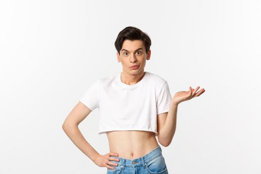 Handsome androgynous man in crop top looking confused, shrugging clueless, standing over white background.