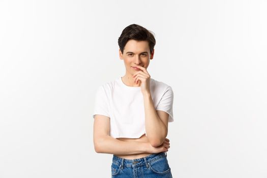 Lgbtq and pride concept. Satisfied young gay man thinking, having an idea and smiling while staring at camera, wearing crop top, white background.