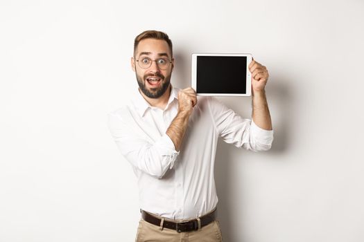 Shopping and technology. Handsome man showing digital tablet screen, wearing glasses with white collar shirt, studio background.