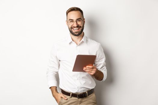 Confident business man holding digital tablet and smiling, standing against white background.