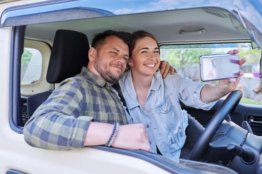 Happy married couple taking selfie photo on smartphone, husband and wife sitting in car.