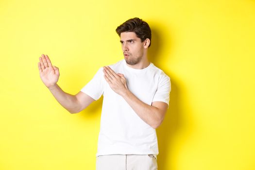 Man showing kung-fu skills, martial arts ninja movement, standing in white t-shirt ready to fight, standing over yellow background.