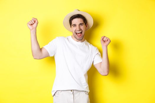 Concept of tourism and lifestyle. Happy man tourist celebrating, rejoicing over vacation, standing over yellow background.