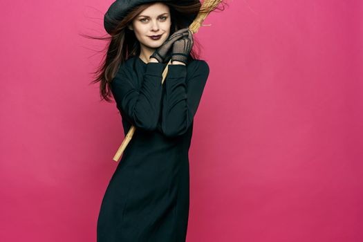 woman in black suit witch broomstick posing pink background. High quality photo